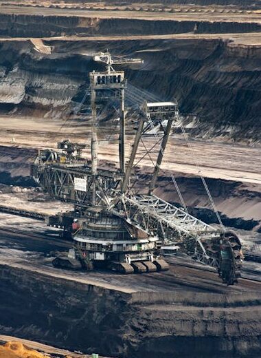 Large bucket wheel excavator operating in an open-pit mine with layered soil and coal.